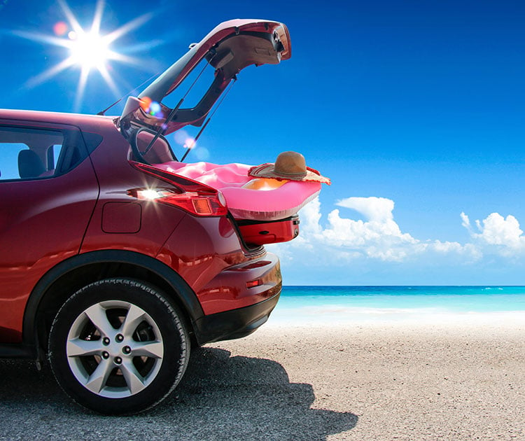 Car hatch open with beach toys parked on beach.