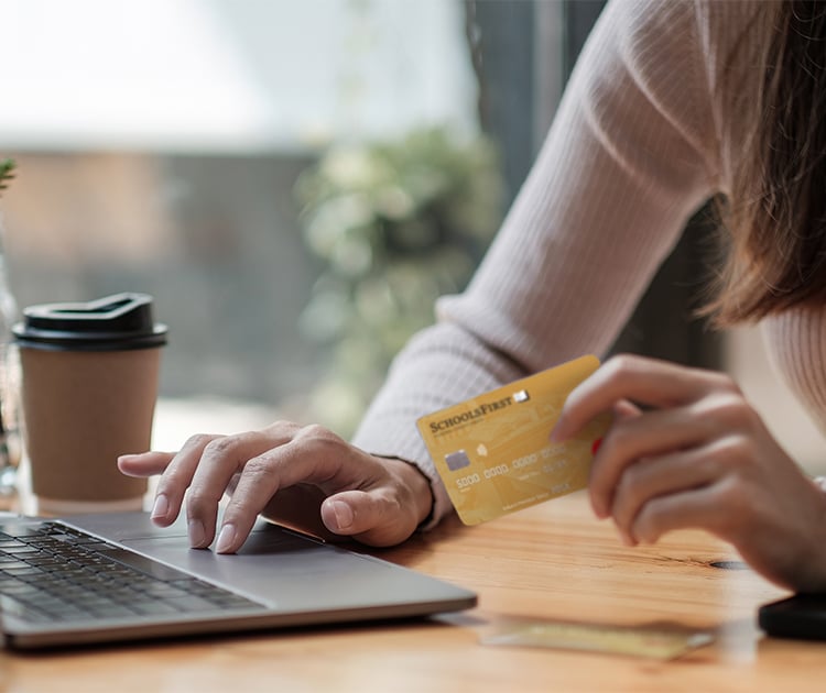 Person at a laptop holding a SchoolsFirst FCU Share-Secured Mastercard.