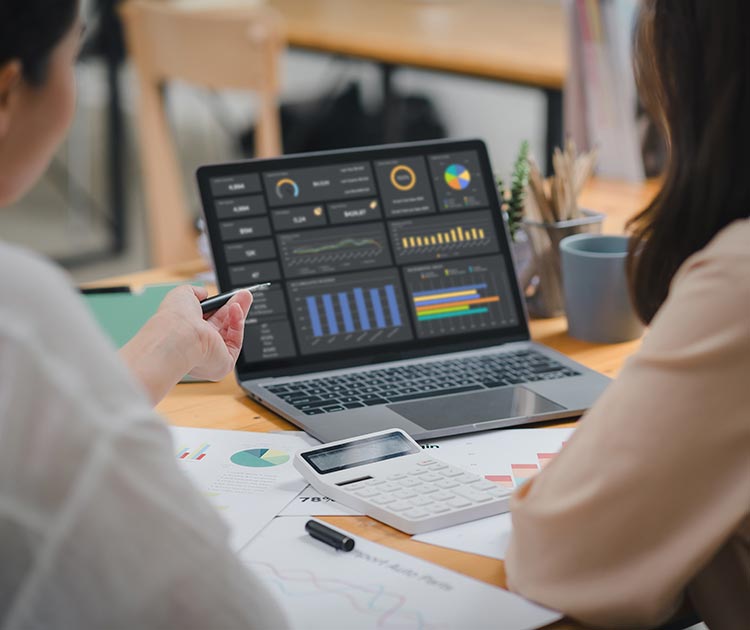 Two businesspersons analyzing data charts, graphs, and a dashboard on a laptop screen.