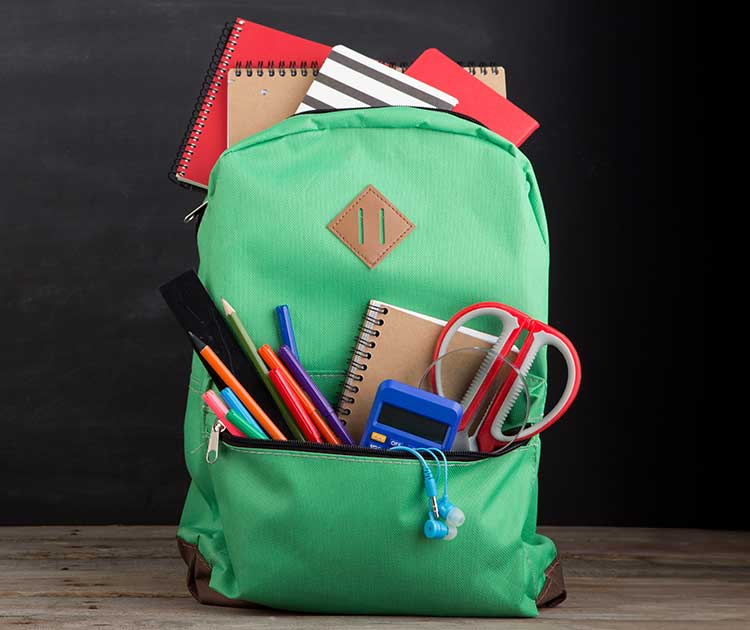 A green backpack overfilled with school supplies.