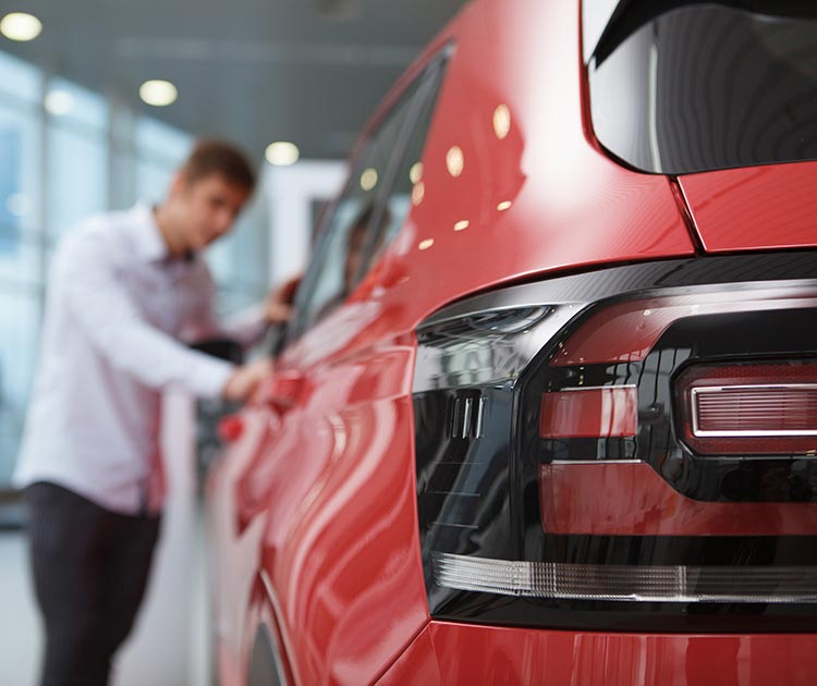 Selective focus on car lights, potential buyer examining auto at the dealership on background.