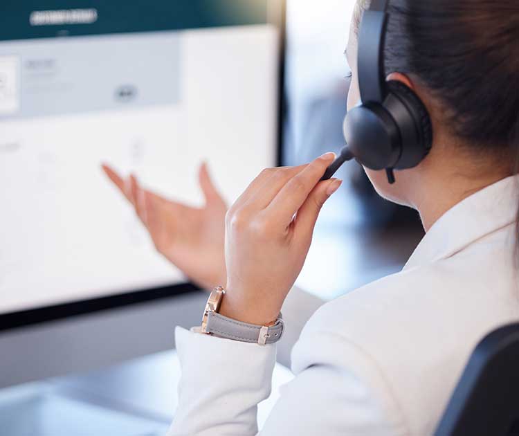 Female agent talking into a headset in front of a desktop computer.