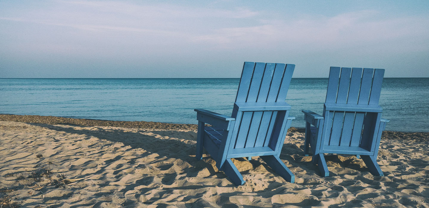 Empty beach chairs on sand facing the ocean.