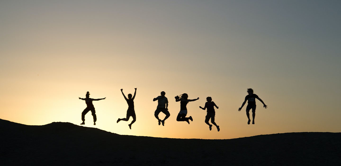 Silhouette of six people jumping against a sunset.