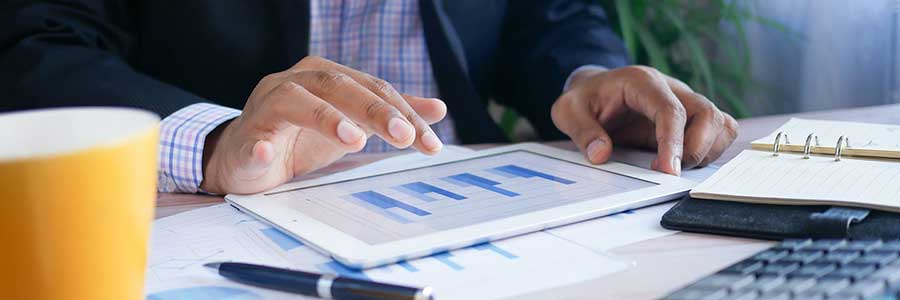 Image of person using a tablet resting on top of financial documents on a desk.