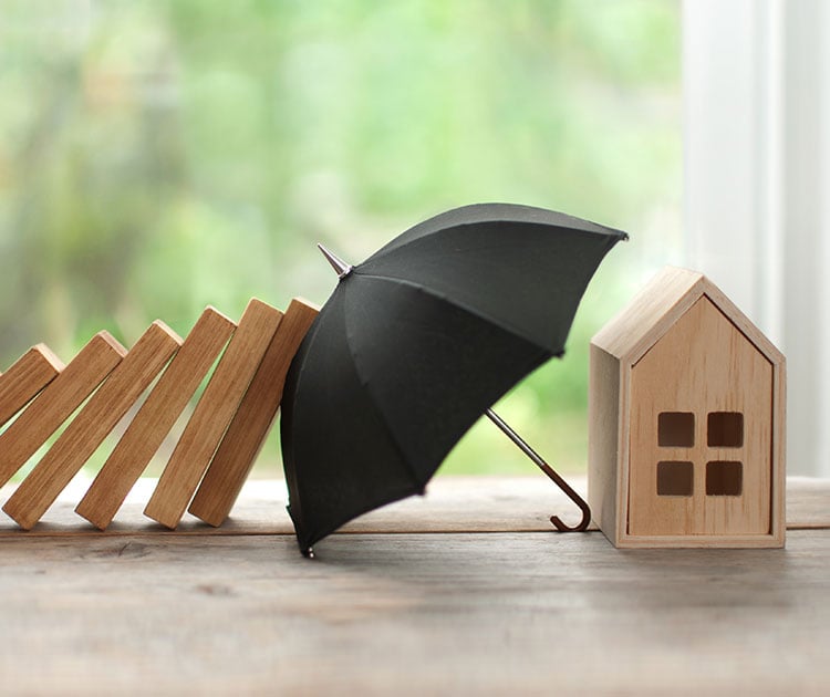 Toy home protected by an umbrella against tilting blocks.