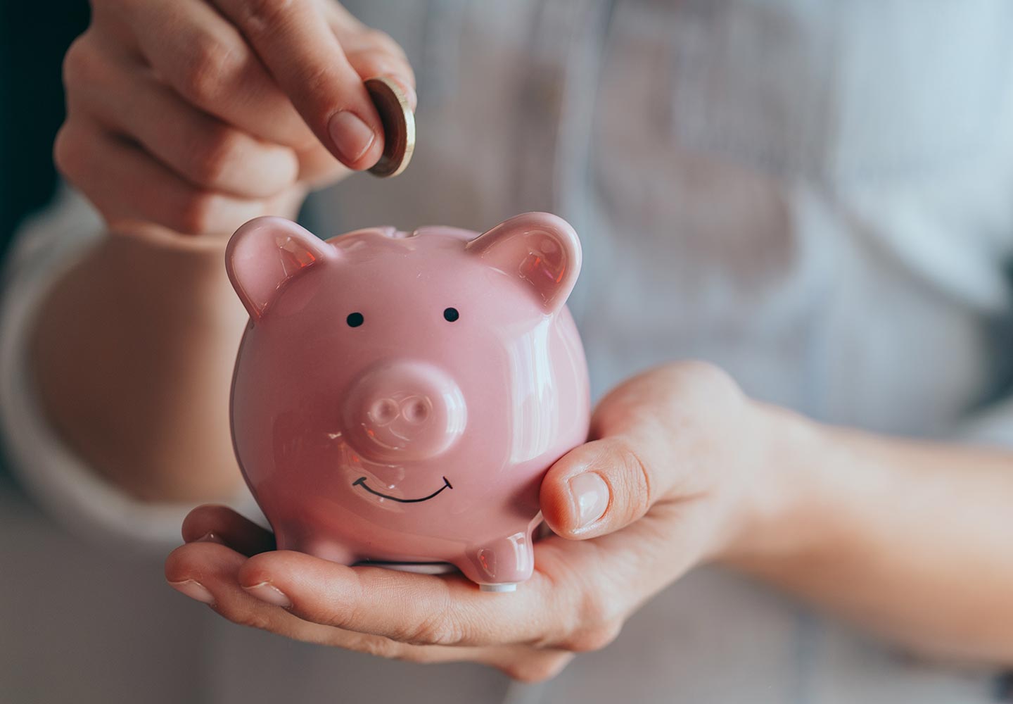 Hands hold a pink piggy bank and puts a coin there.