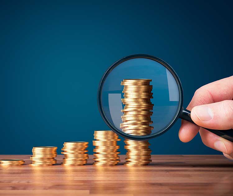 A magnifying glass in front of a row of stacked coins.