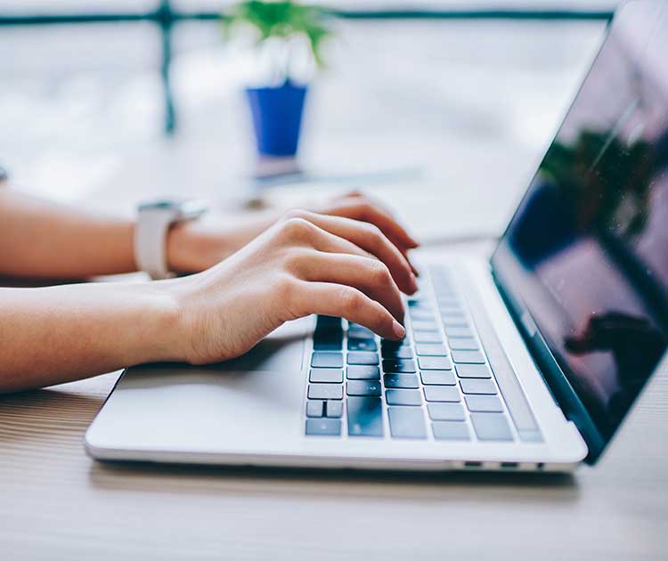 Female hands typing on laptop computer searching online.